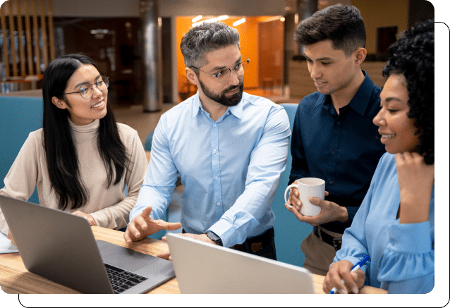 Four colleagues discussing a project over a laptop in a modern office setting.