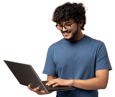 A smiling young man with curly hair and glasses using a laptop computer.