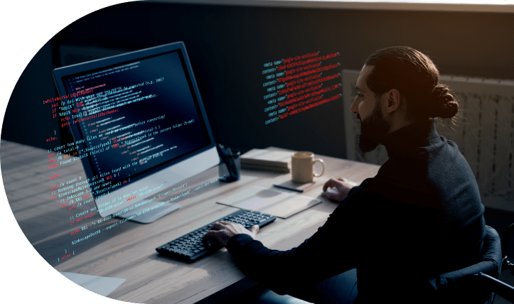 A software developer working on code at a computer workstation in a dimly lit office environment.